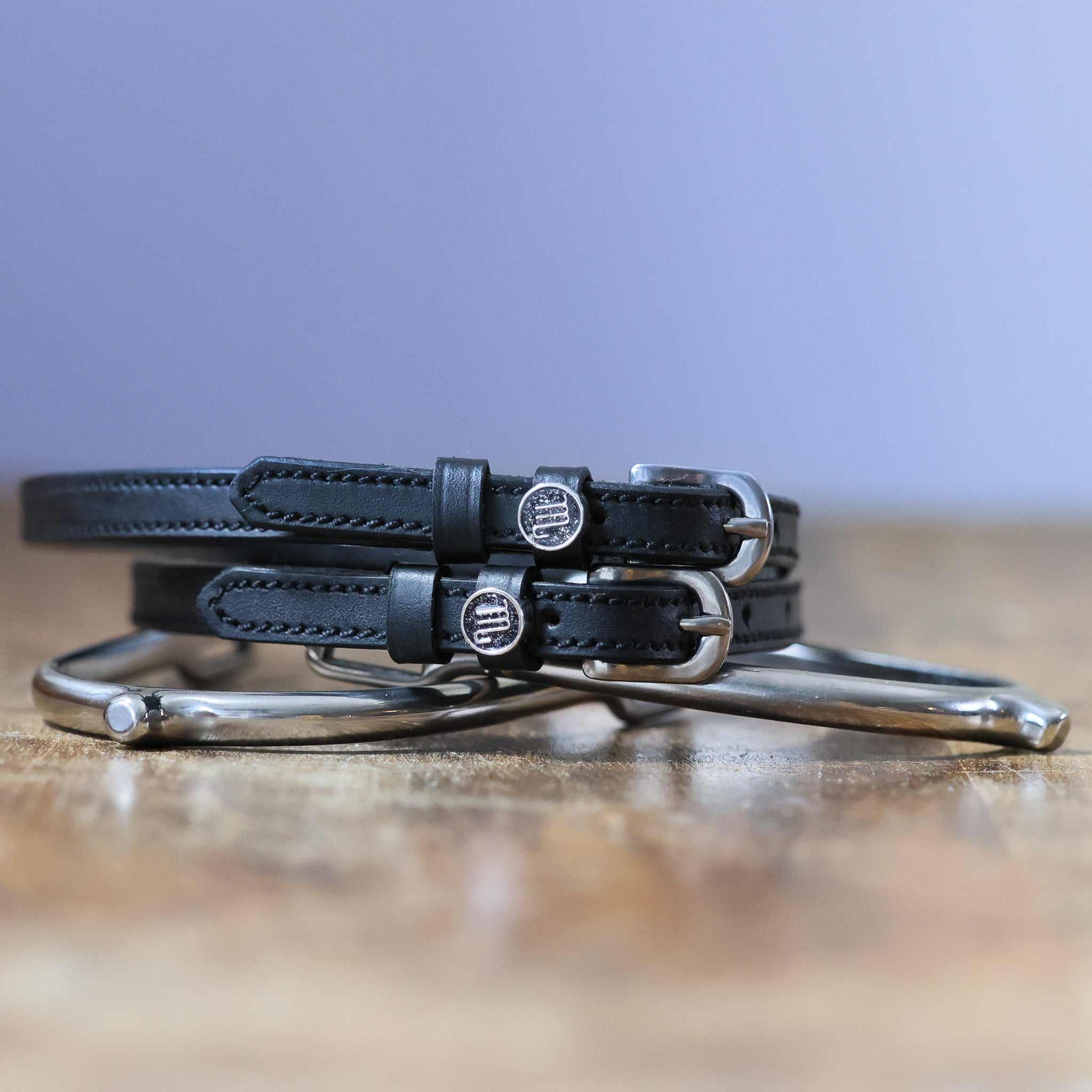 Black leather Scorpio Spur Straps with stainless steel buckles and custom charms on wooden surface