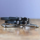 Black leather Scorpio Spur Straps with stainless steel buckles and custom charms on wooden surface