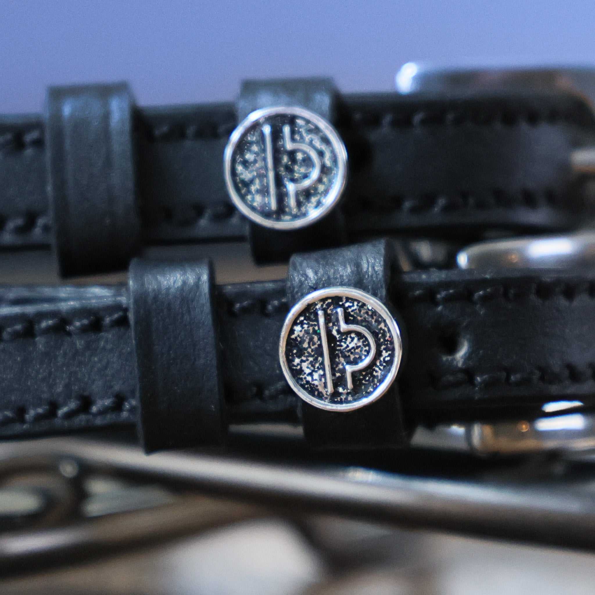 Close-up of black leather Libra Spur Straps with custom silver charm and stainless steel buckle