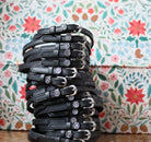 Zodiac Bundle of black leather spur straps with zodiac sign charms stacked against floral background