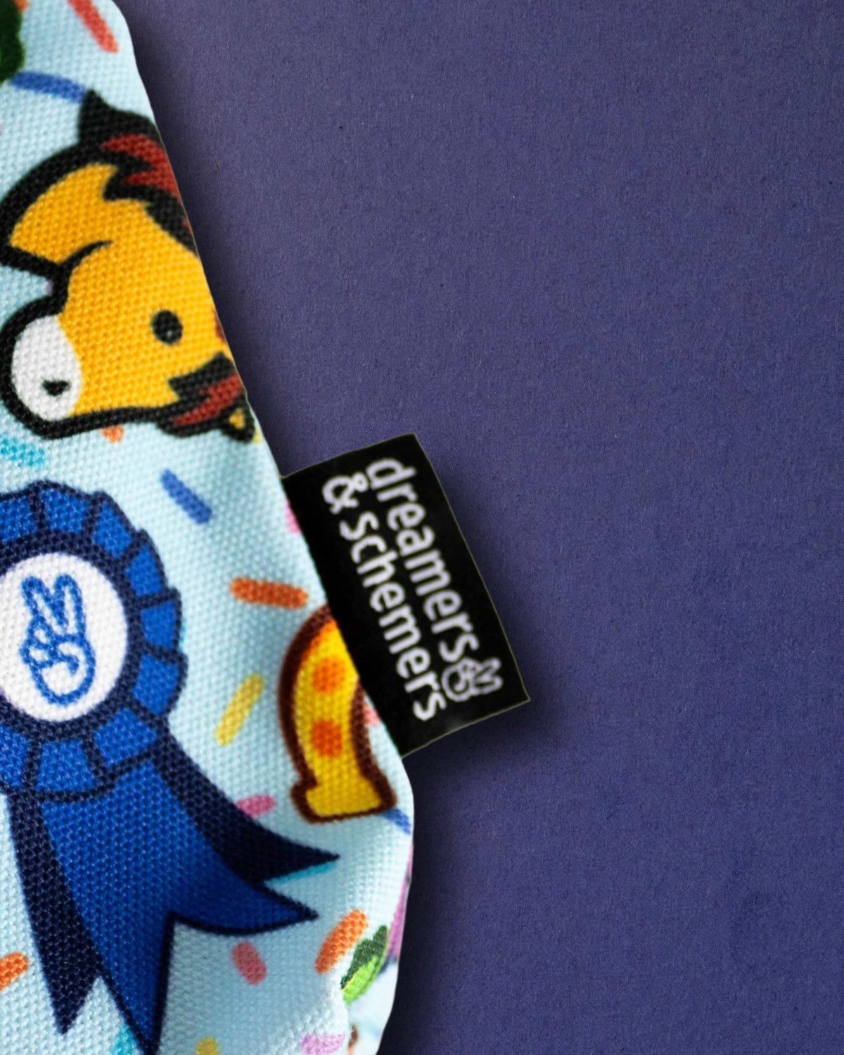 Woven dreamers & schemers tag on the Lucky Charm pouch, next to a printed blue prize ribbon