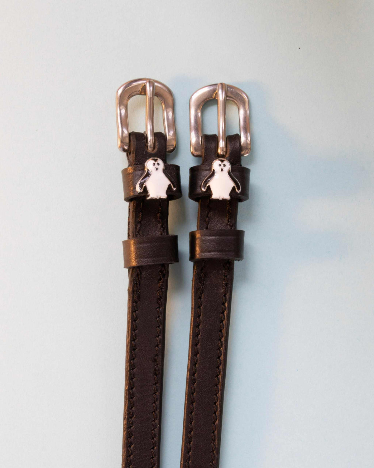 Penguin ManeJane spur straps with the signature Penguin charm, shown on an off-white background