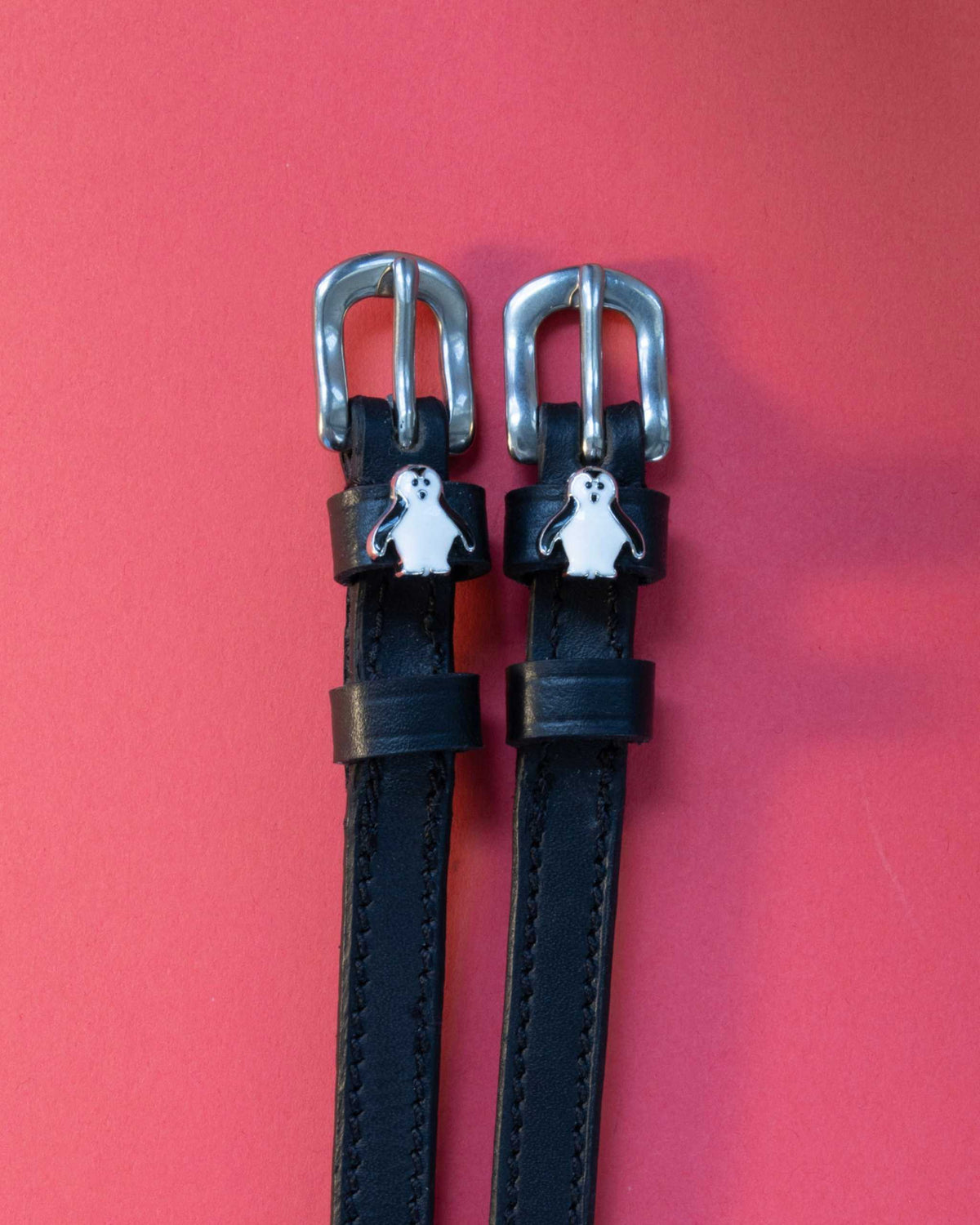 Penguin ManeJane spur straps with the signature Penguin charm, shown on a coral background