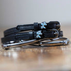 Black leather Balloon Puppy Spur Straps with stainless steel buckles and custom puppy charms on wooden surface