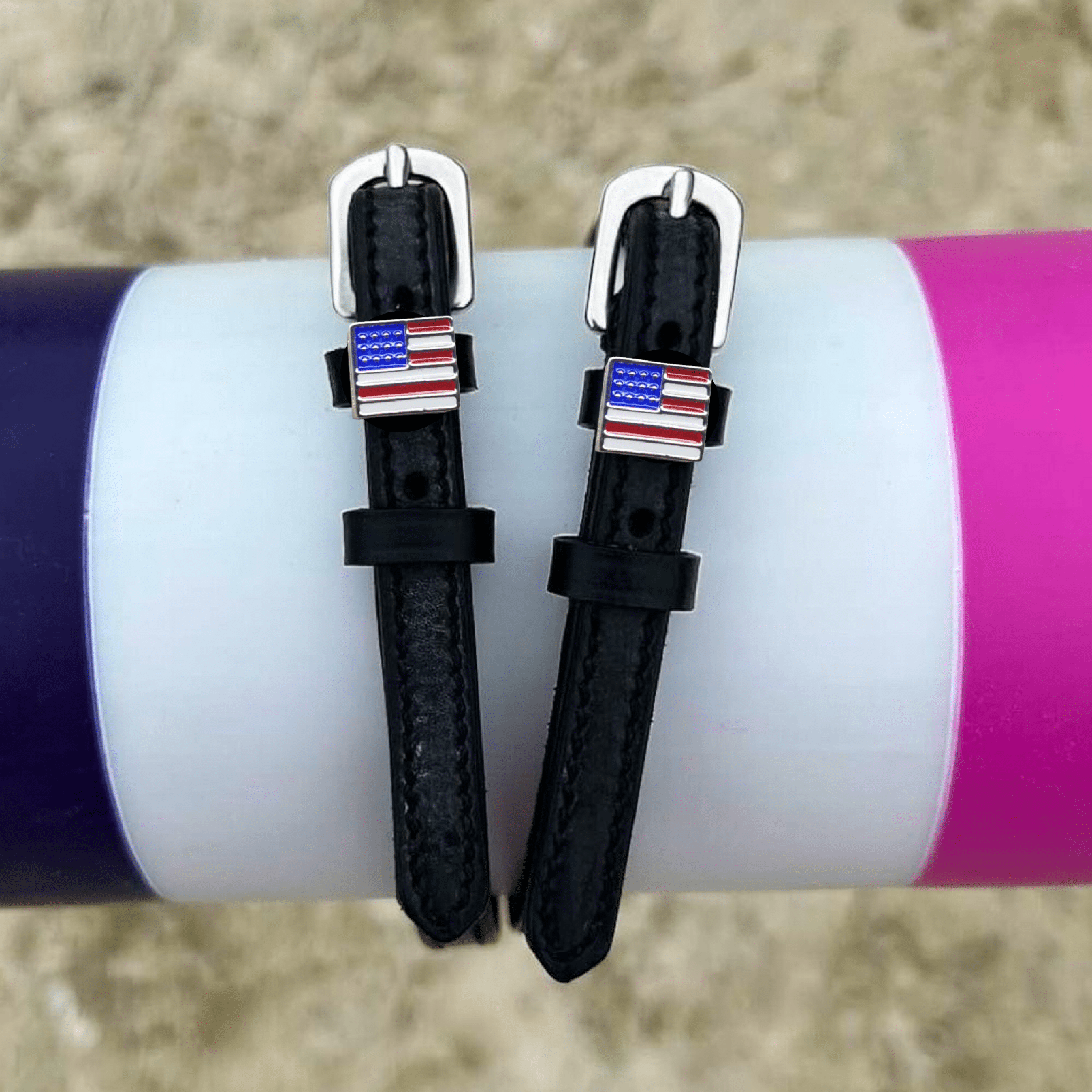 Black leather American flag spur straps draped over a colorful jump pole