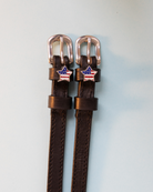 Brown leather American-flag star spur straps with rose-gold buckles, flat-lay