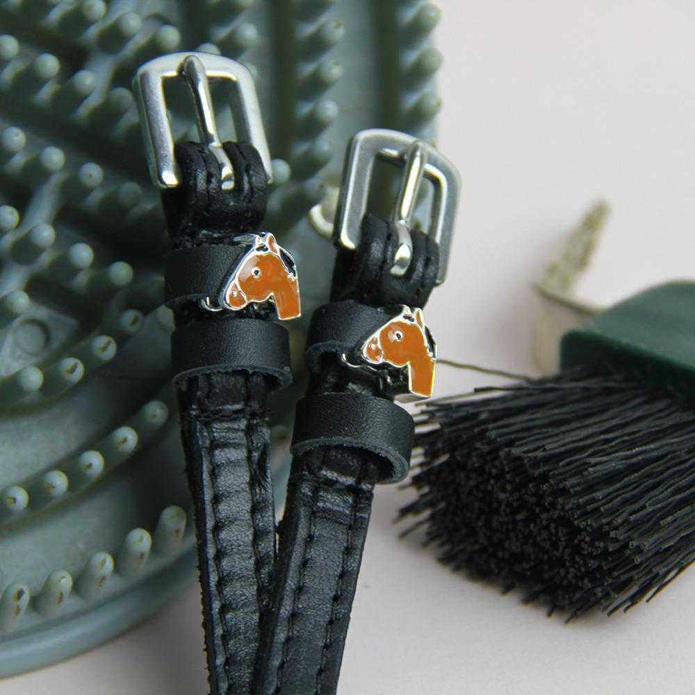 Black leather horse-head spur straps beside horse grooming brushes and curry comb