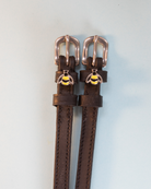 Brown leather bee spur straps with rose-gold buckles and bumblebee charms, flat-lay