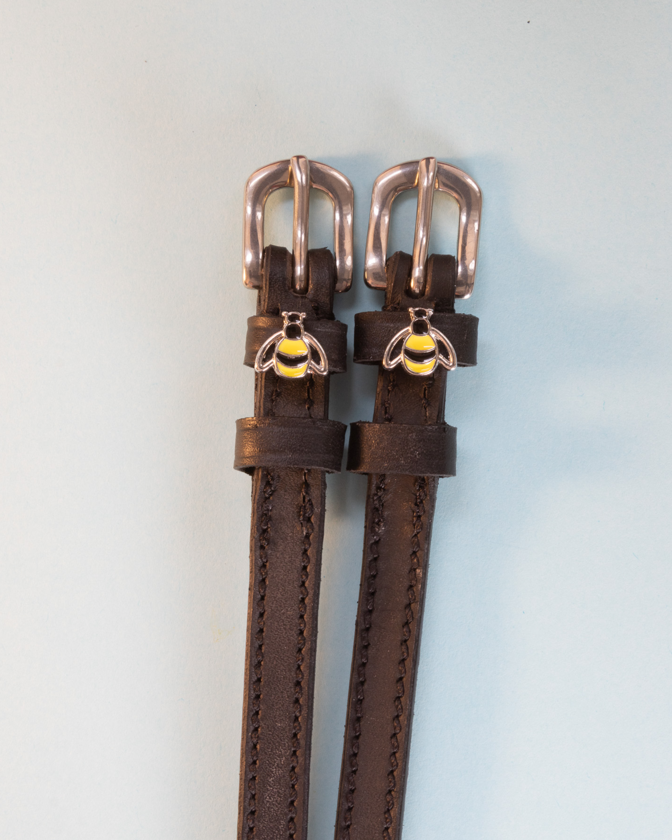Brown leather bee spur straps with rose-gold buckles and bumblebee charms, flat-lay