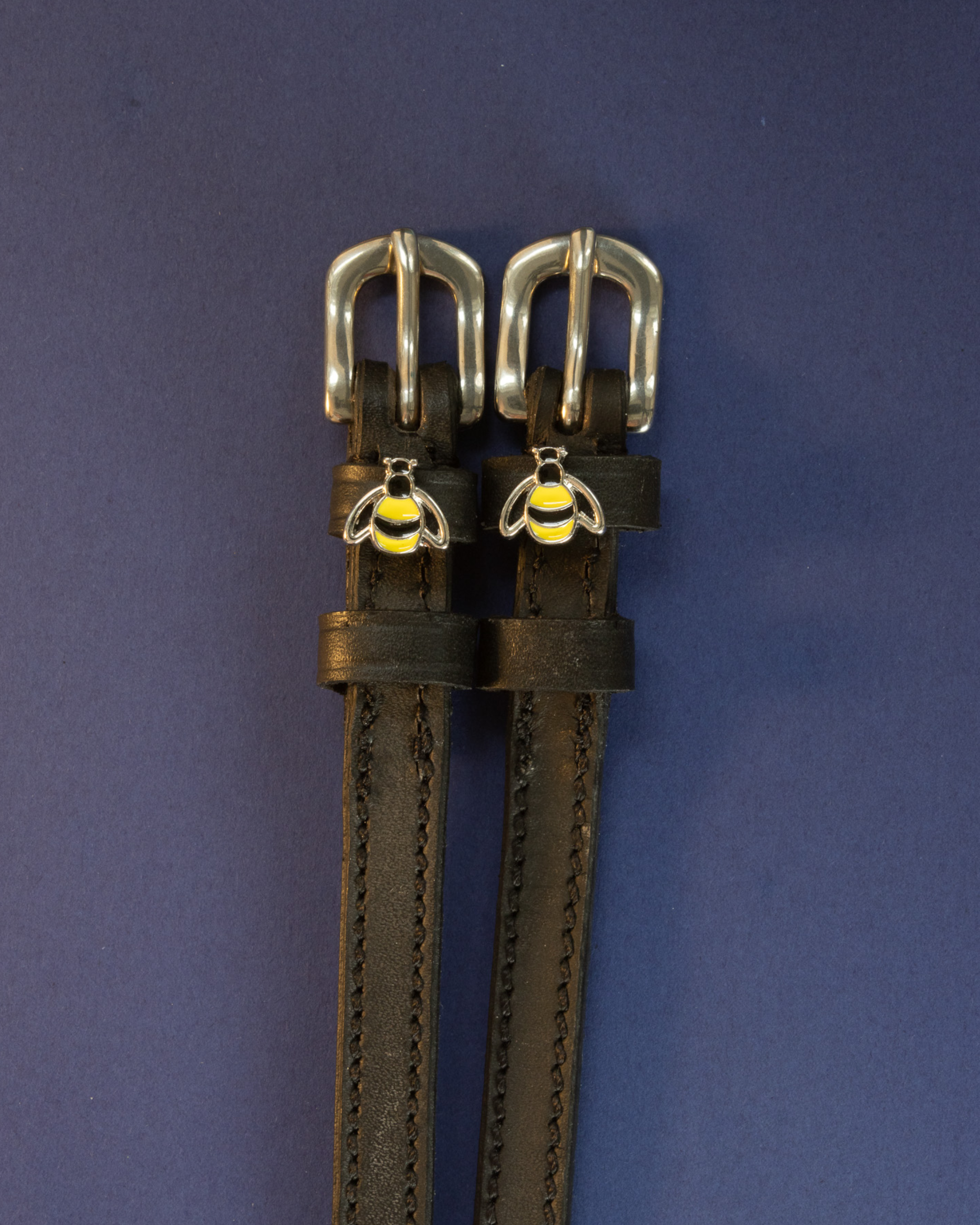 Pair of black leather bee spur straps with silver buckles laid flat on a navy blue background