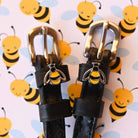 Bumblebee charms on black leather spur straps against a cartoon bee print backdrop
