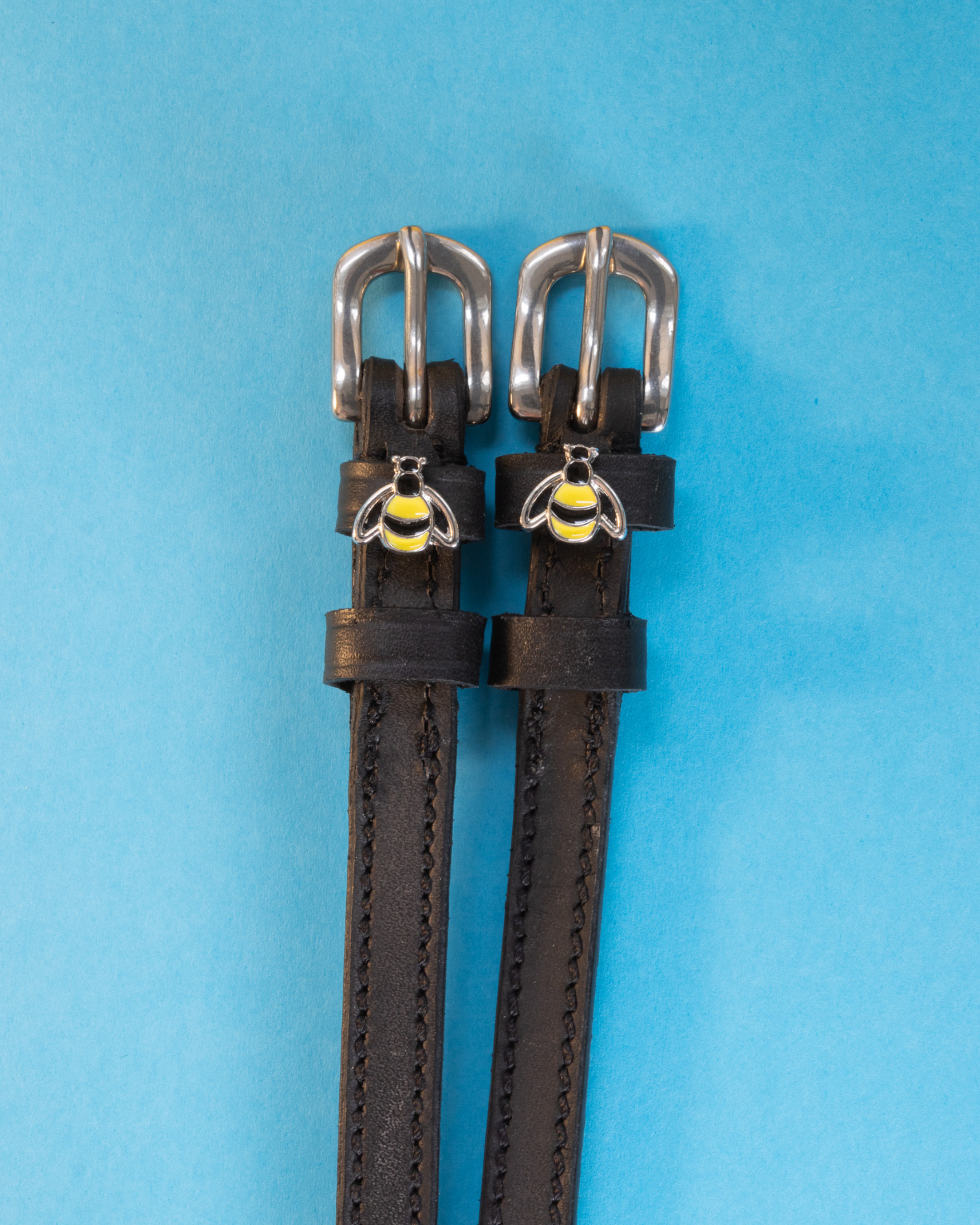 Black leather bee spur straps with silver buckles and enamel bee charms on light blue