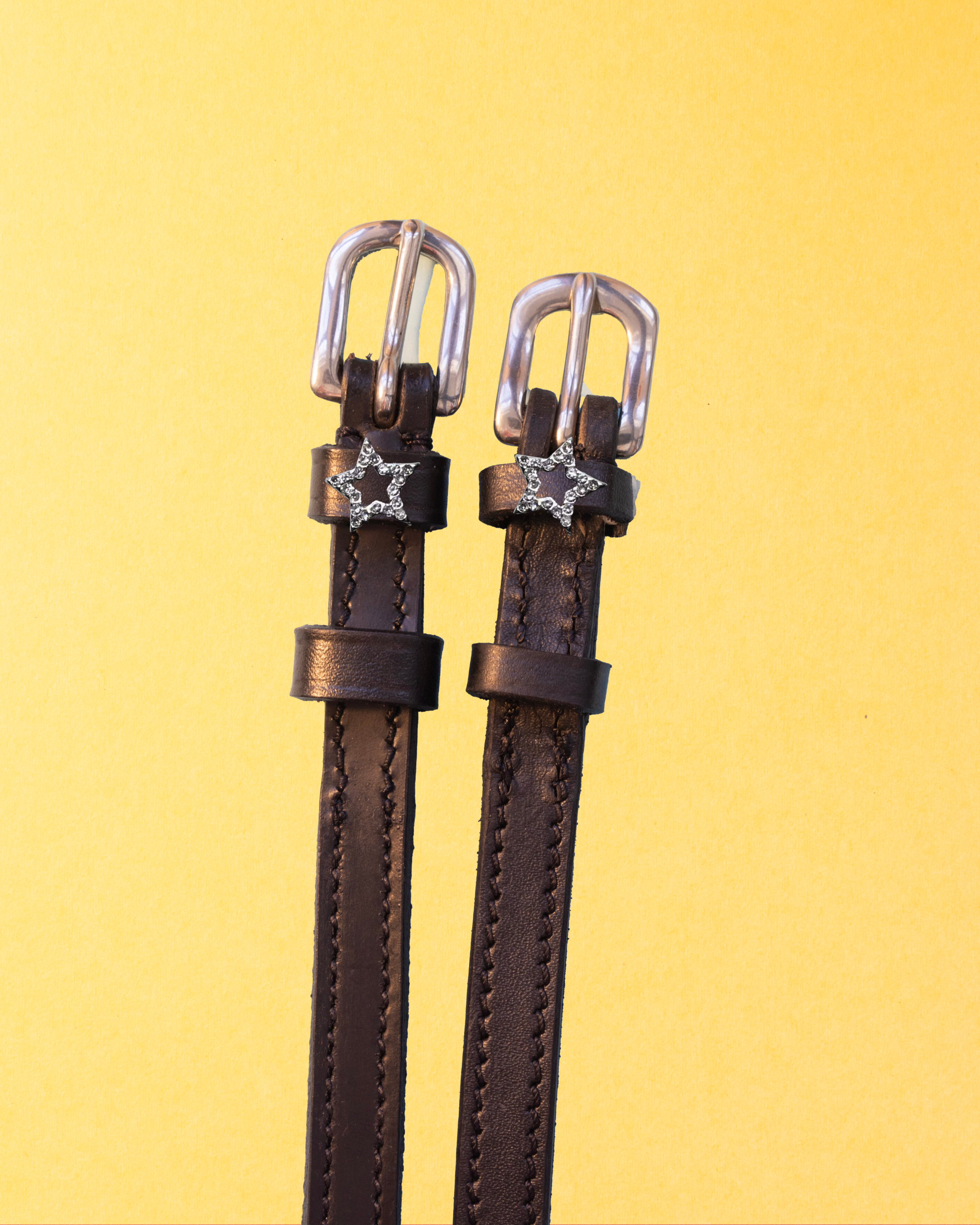 Rhinestone star outline spur straps flat-laid on a yellow background