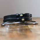 Coiled black leather burrito spur straps stacked on a silver spur on a wooden table