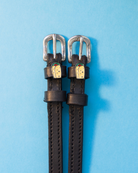 Pair of black leather spur straps with burrito charms flat-laid on a light blue background
