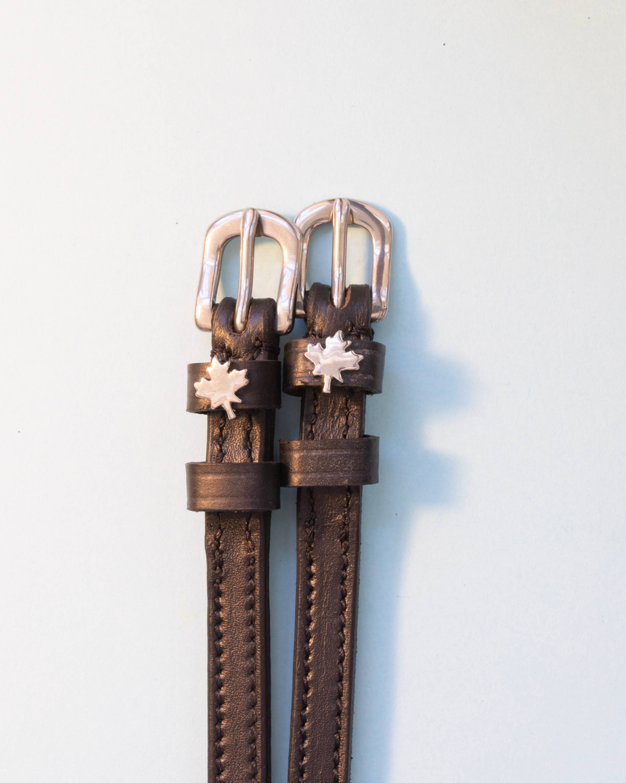 Dark brown leather maple leaf spur straps with silver buckles on a pale background