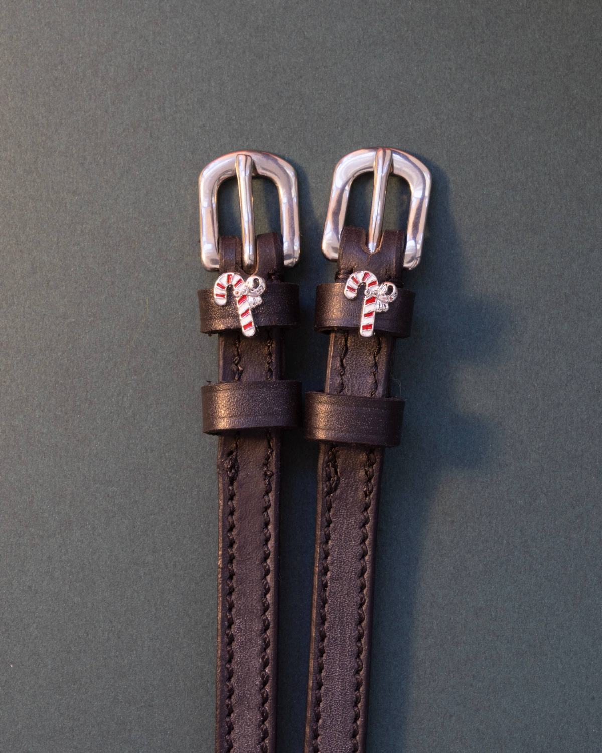 Black leather ManeJane spur straps with red-and-white candy cane charms on slate grey