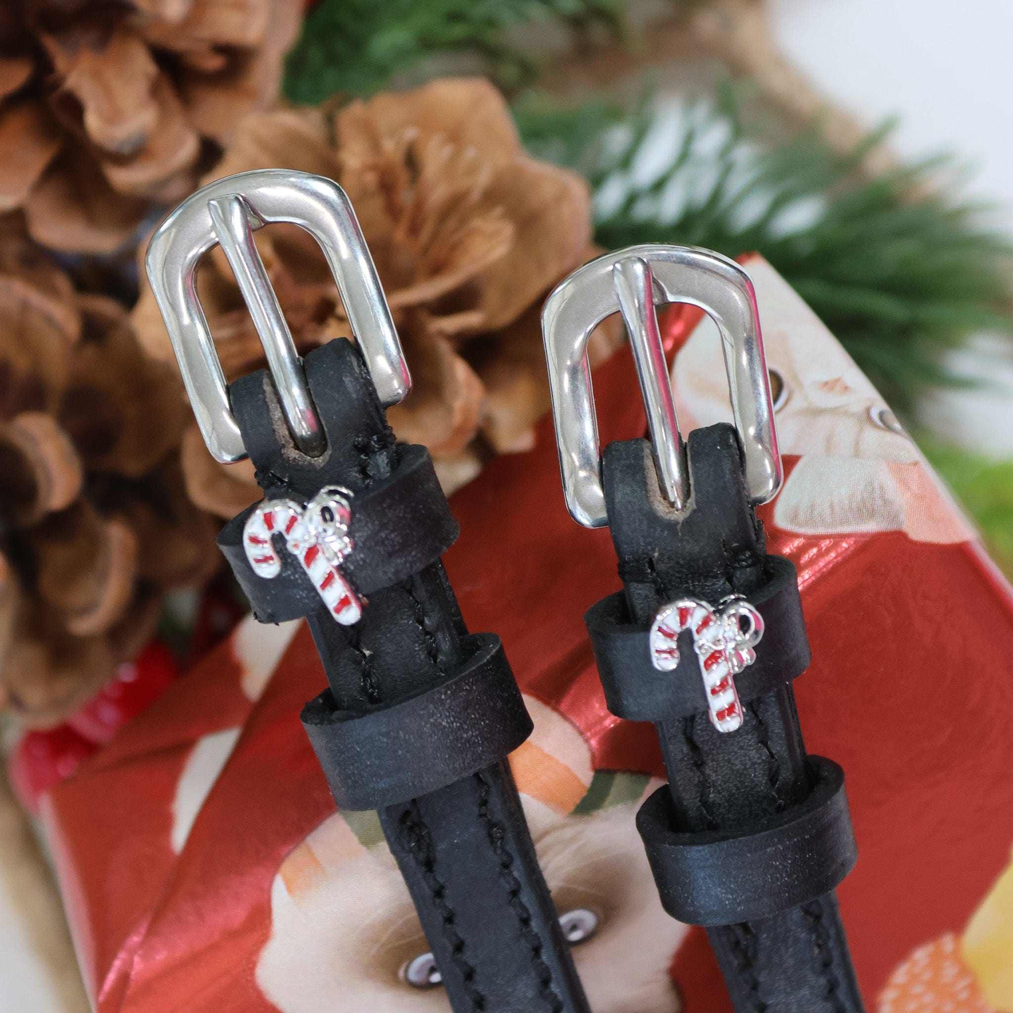 Silver buckles and candy cane charms of spur straps on a festive pinecone setting