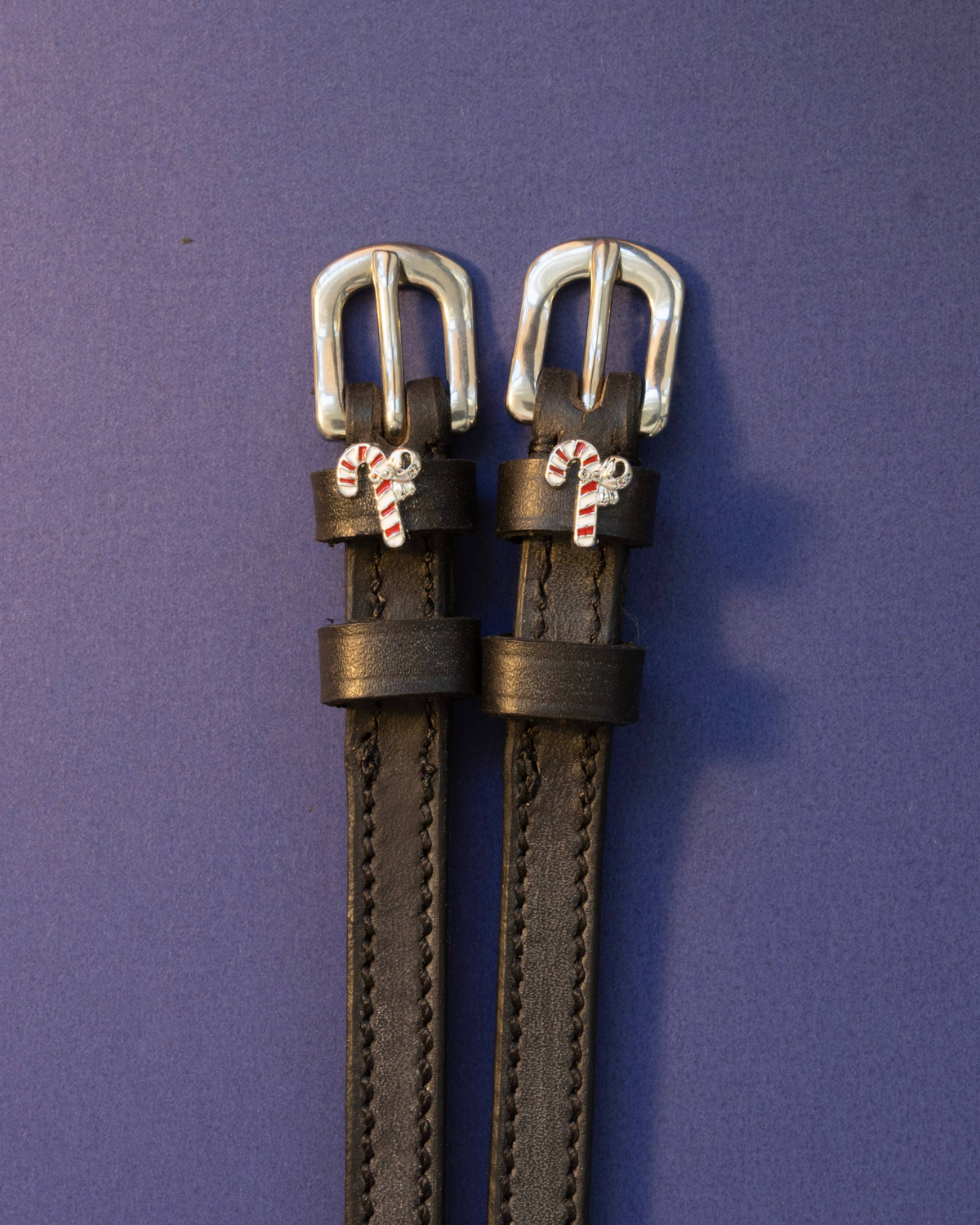 Candy cane spur straps in black leather with silver buckles on a periwinkle background