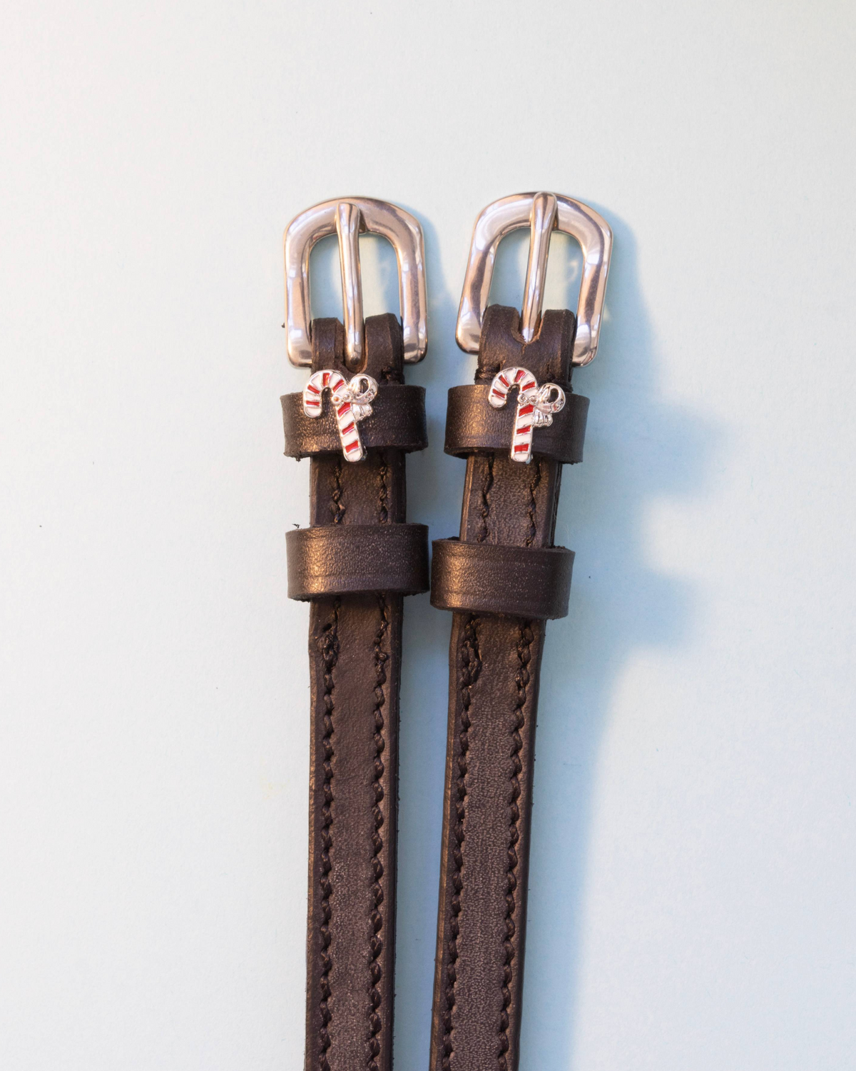 Dark brown leather ManeJane candy cane spur straps with silver buckles on grey