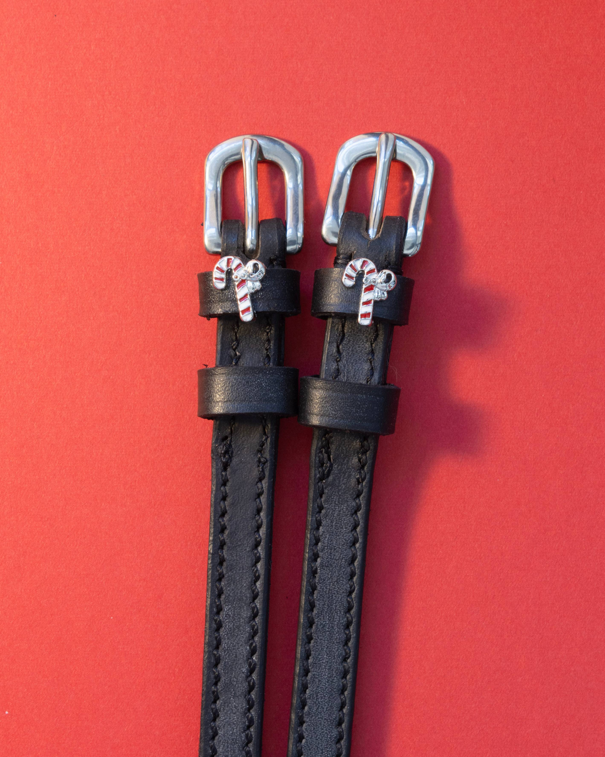 Pair of black leather candy cane spur straps with silver buckles on a red background