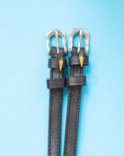 Black leather carrot spur straps with silver buckles flat-laid on a light blue background