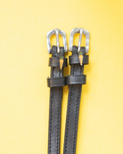 Pair of black leather ManeJane carrot spur straps with silver buckles on a yellow background