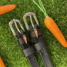 Black leather carrot spur straps styled on grass beside real and toy carrots by ManeJane