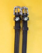 Black leather cash money spur straps flat-laid on a yellow background
