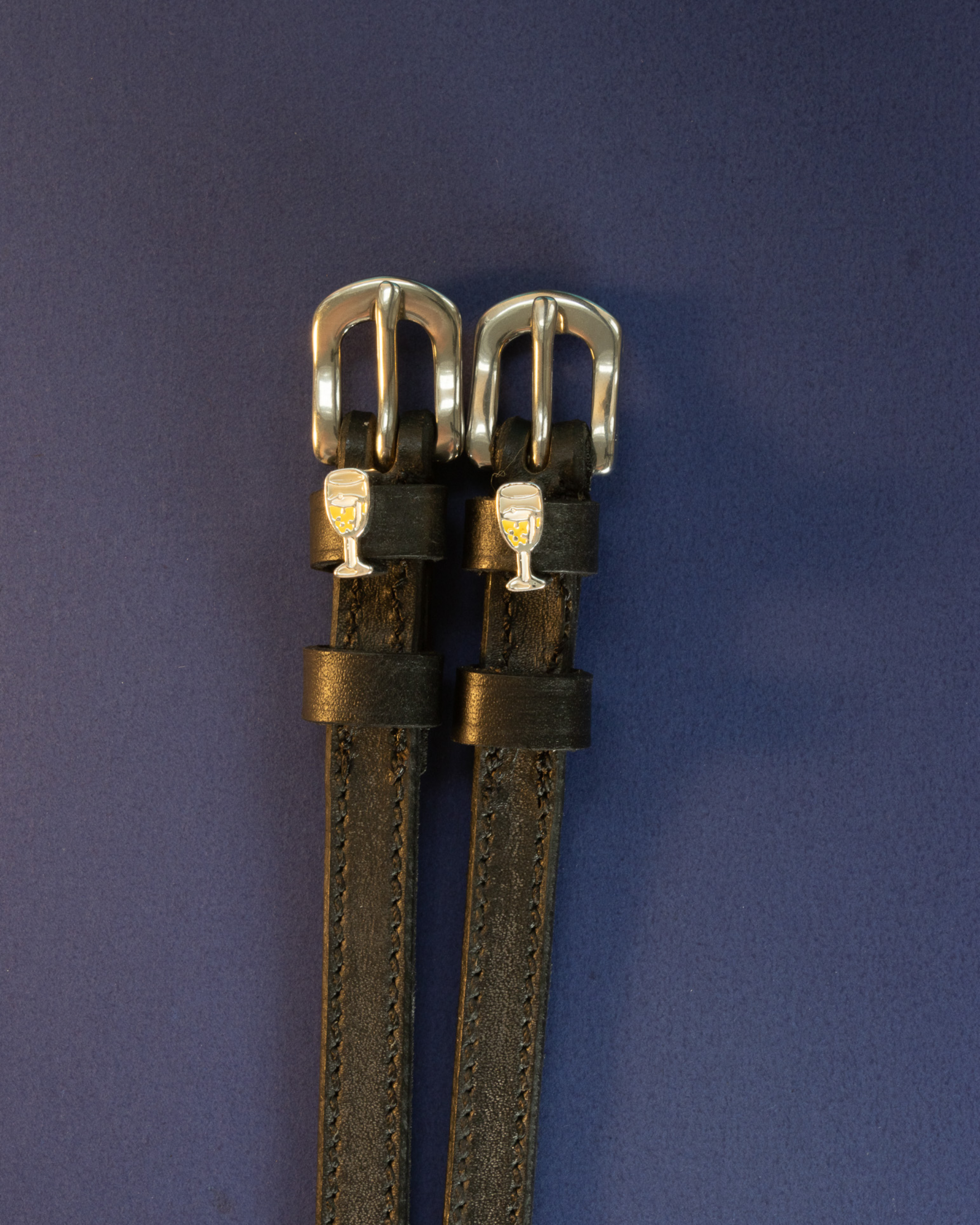 Pair of champagne-glass ManeJane spur straps flat on a navy background