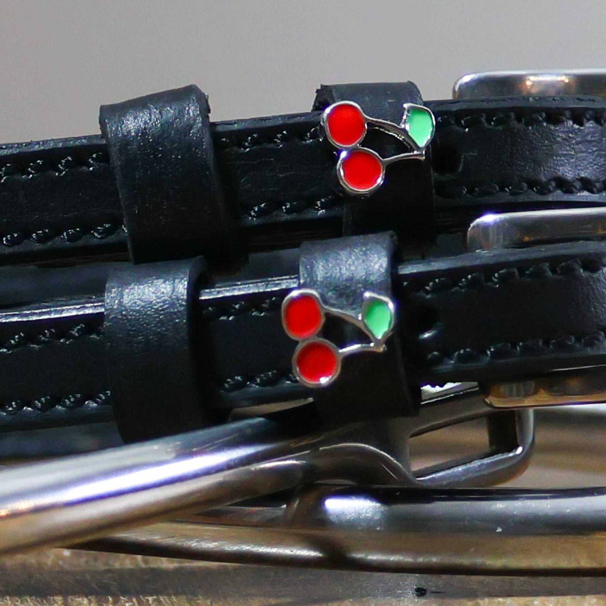 Close-up of a red-and-green enamel cherry charm on a black leather spur strap keeper