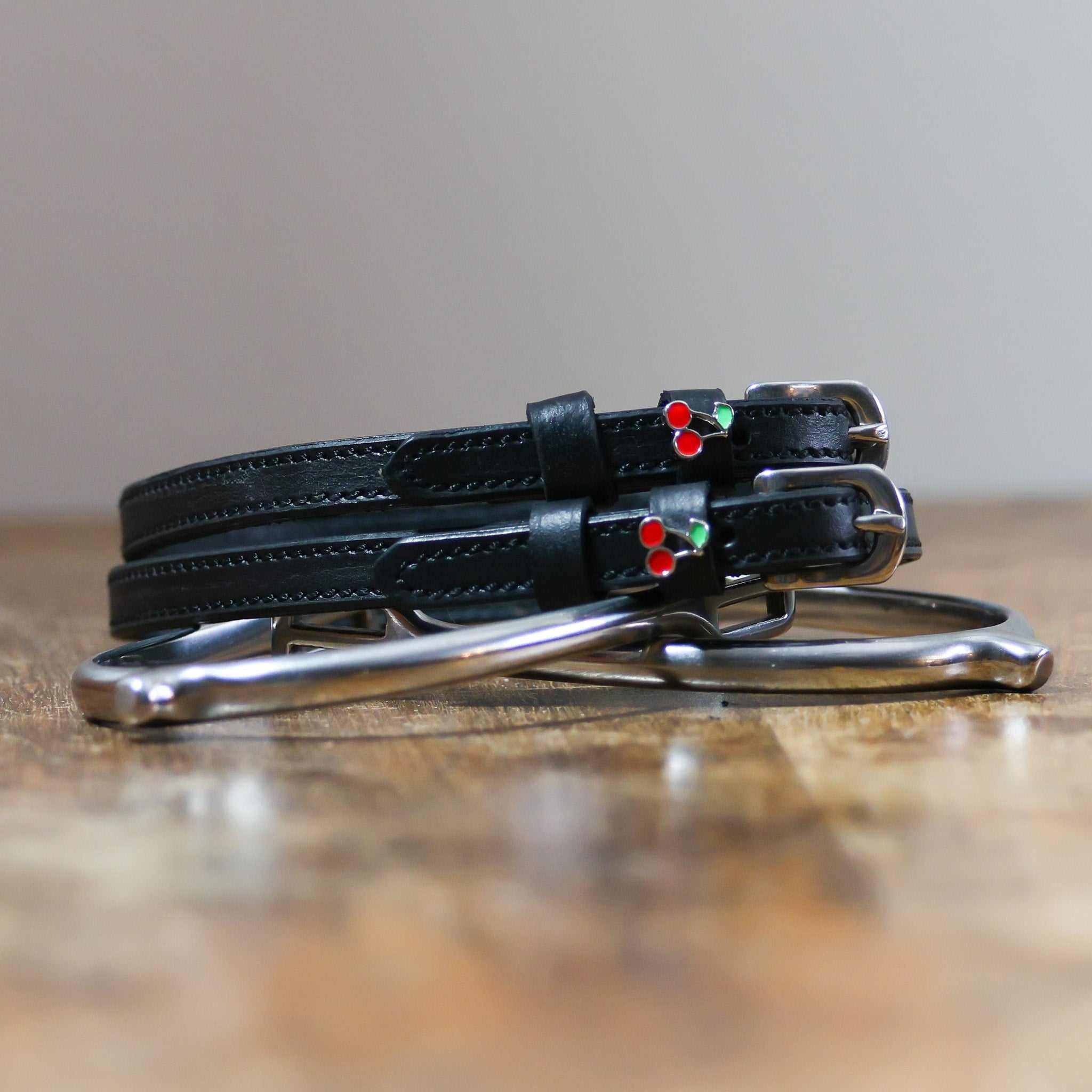 Black leather cherry spur straps coiled beside a metal spur on a wooden surface