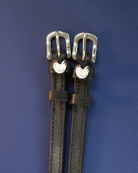 Black leather chicken spur straps with silver buckles on a navy blue background