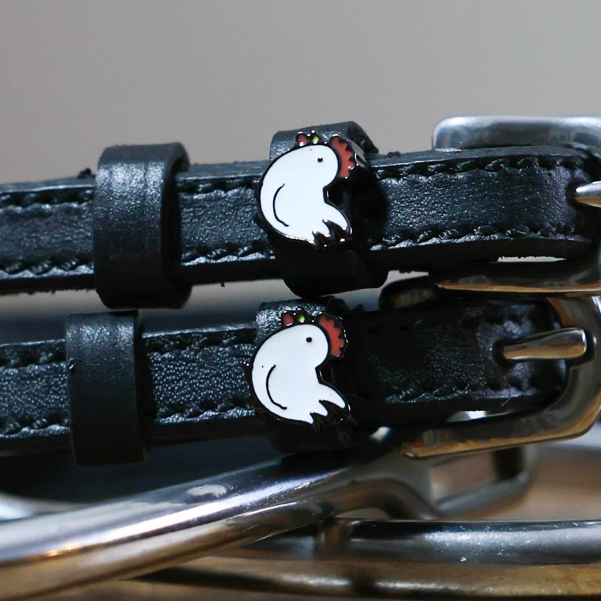 Close-up of white enamel chicken charms on black leather ManeJane spur strap keepers
