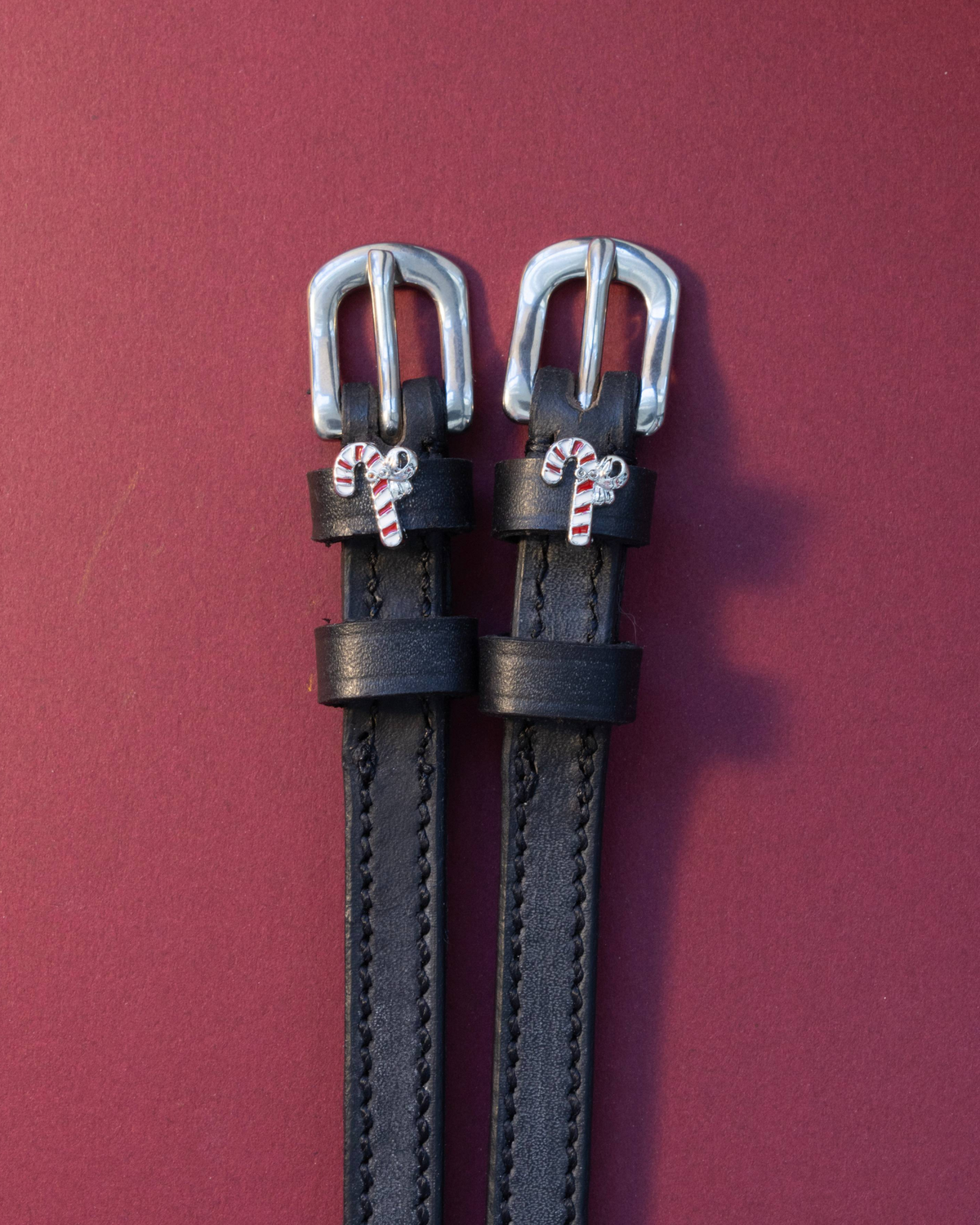 Black leather candy cane charm spur straps with silver buckles on a deep red background