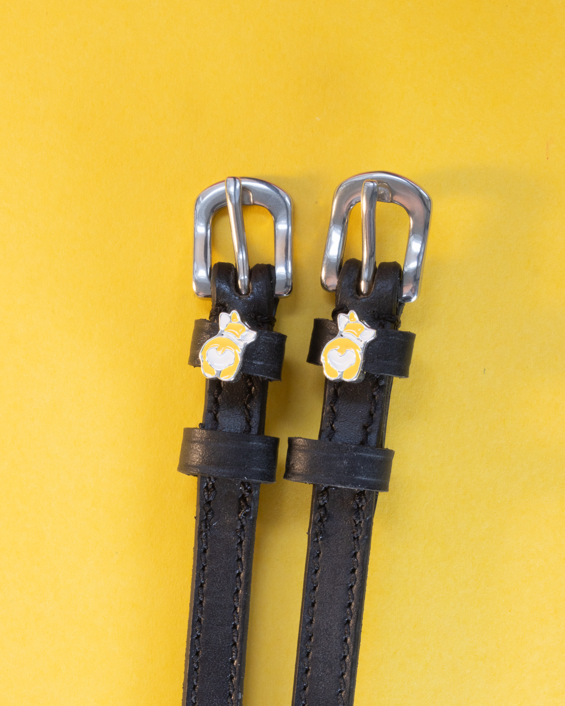 Pair of black leather ManeJane spur straps with corgi butt charms on yellow
