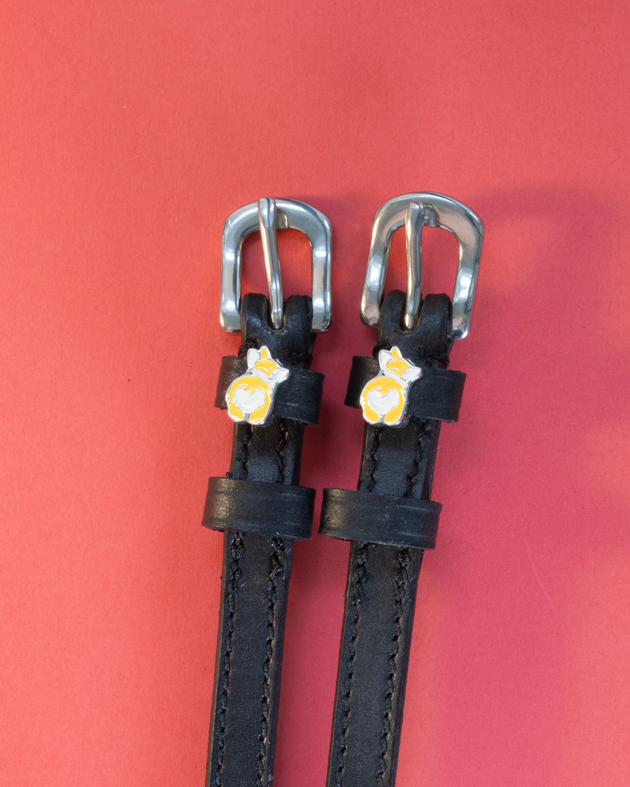 Pair of black leather corgi butt spur straps on a coral background