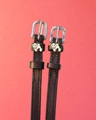 Pair of black leather ManeJane cow spur straps with enamel cow charms on a coral background