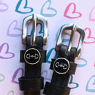 D-ring bit charm spur straps on a pastel heart-doodle backdrop, buckle close-up