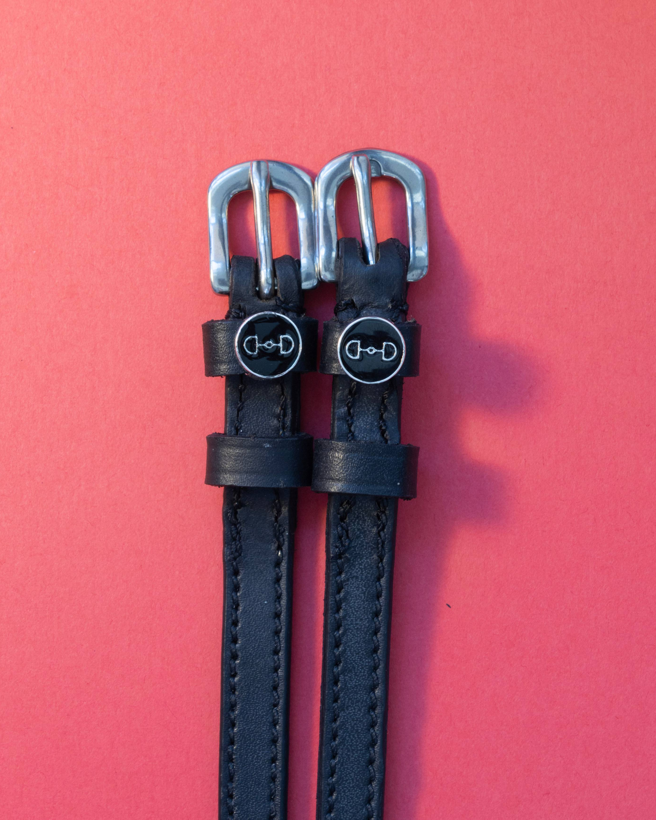 Black leather spur straps with round bit charms flat on a red background