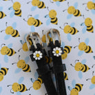 White daisy charm spur straps with silver buckles against a cartoon bee print backdrop
