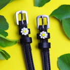 Daisy flower spur straps with silver buckles on yellow framed by green leaves