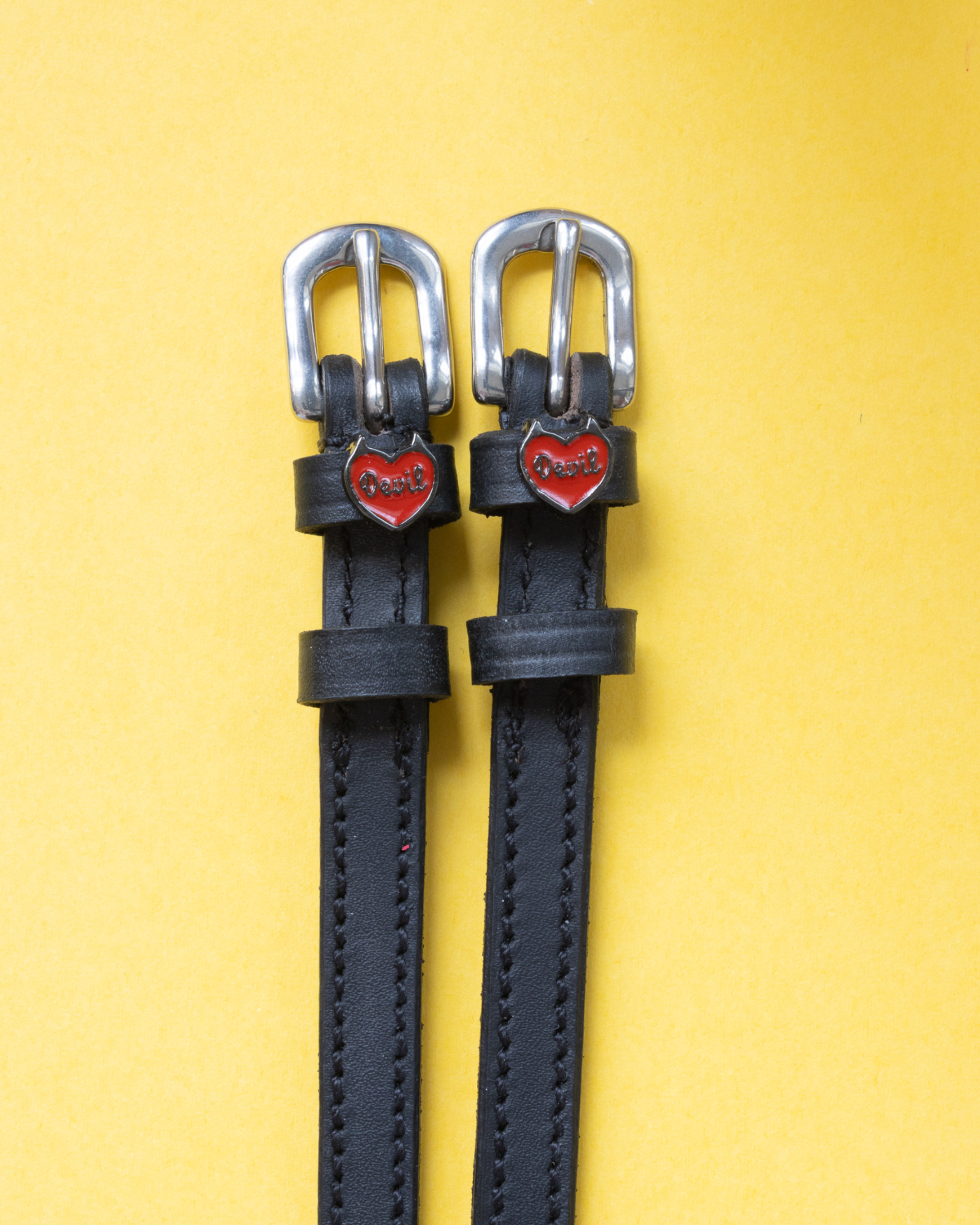 Black leather Devil heart spur straps flat-laid on a bright yellow background