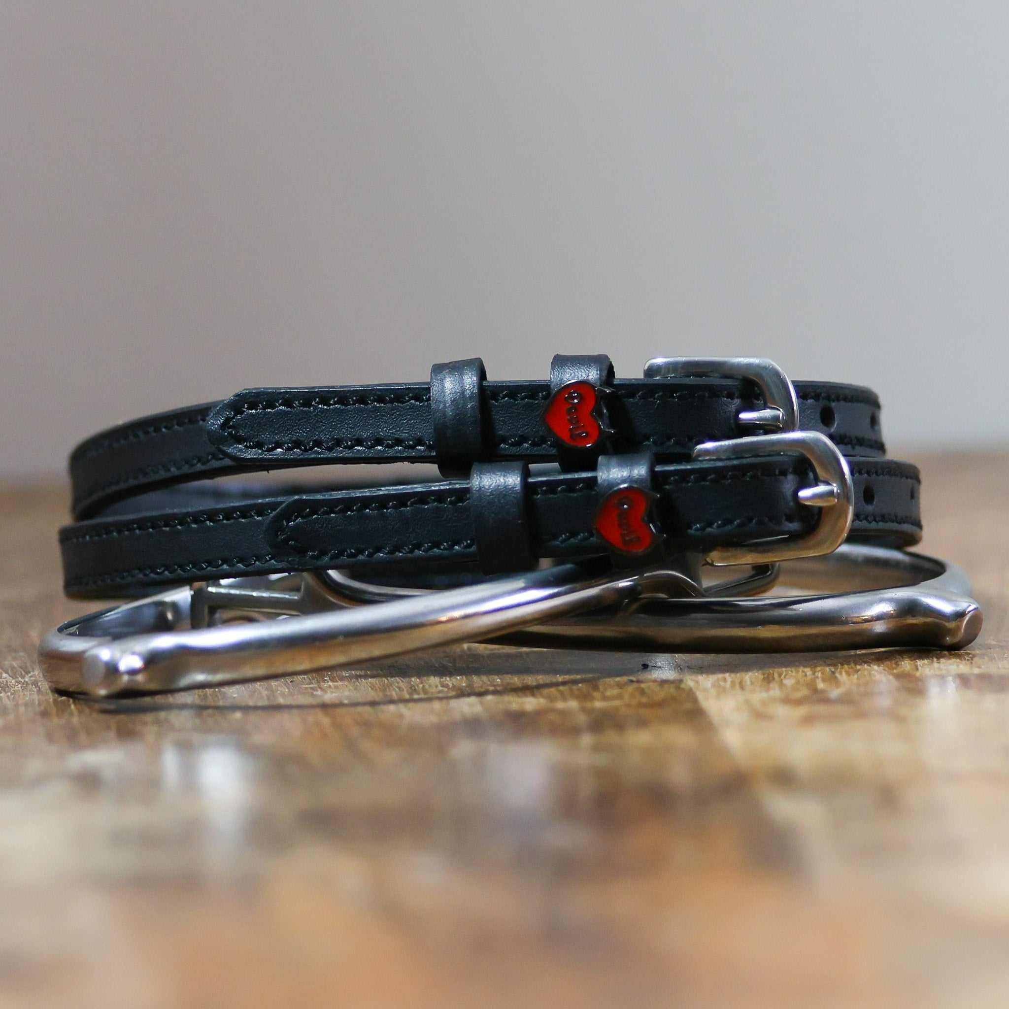Black Devil heart spur straps coiled around a silver spur on a wooden surface