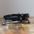 Black leather disco ball spur straps coiled beside a silver spur on a wood surface