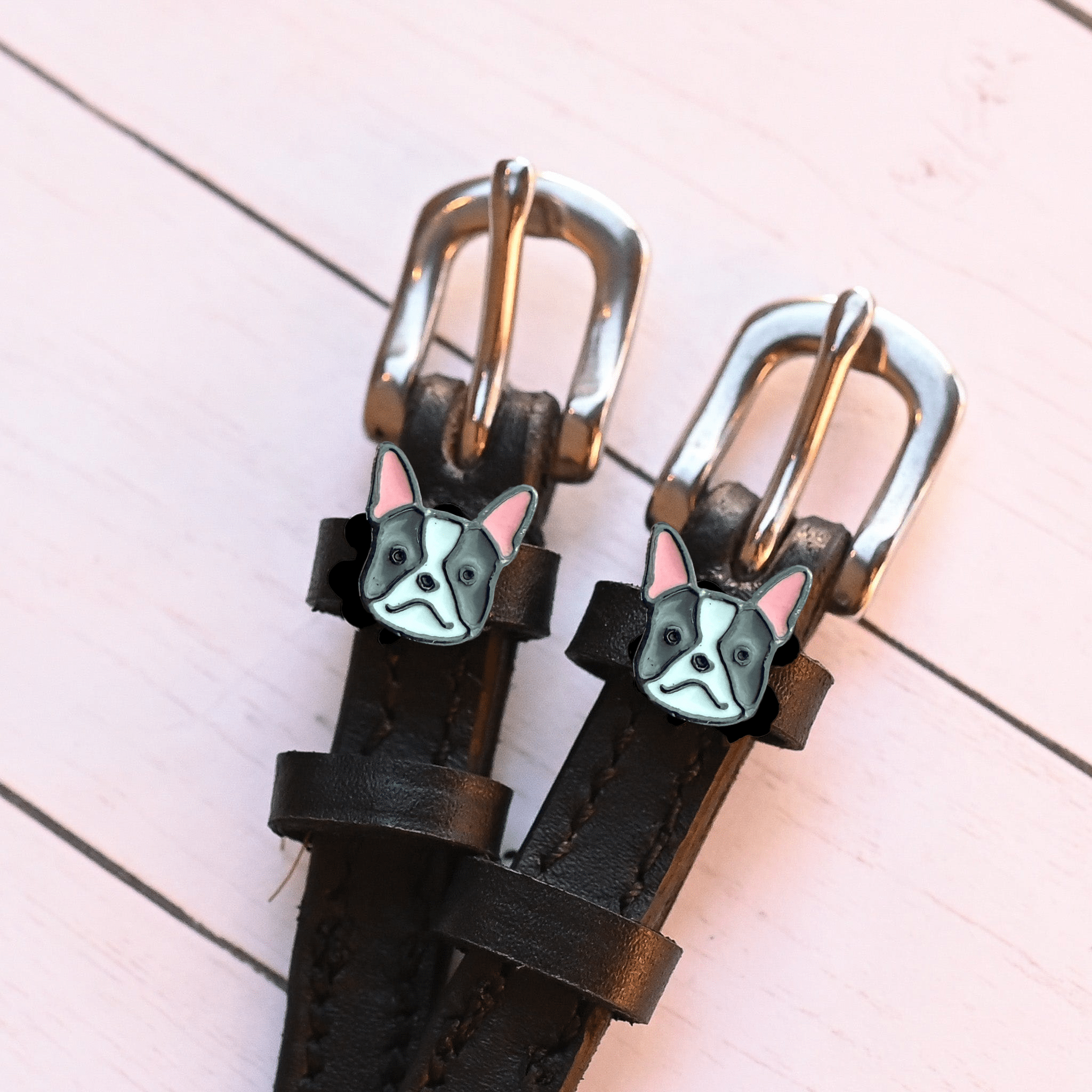 Angled close-up of French bulldog charms on ManeJane spur straps over pink planks