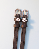 Dark brown ManeJane spur straps with white poodle face charms on off-white