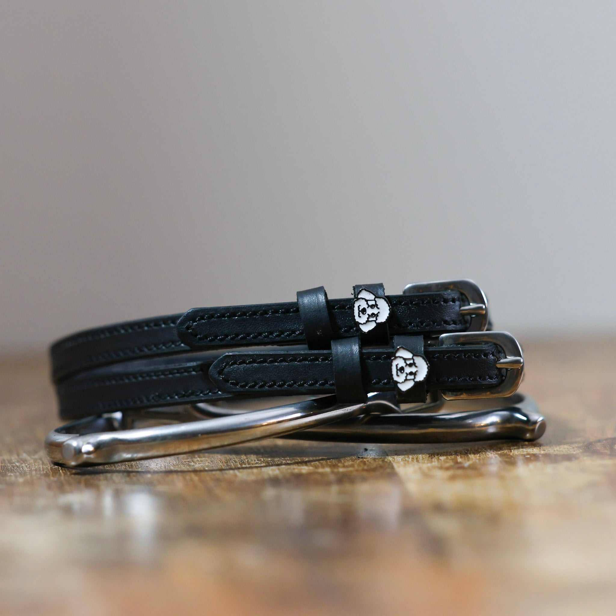 Black leather poodle spur straps stacked on a silver spur on wood, close-up