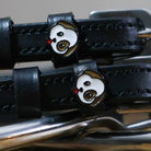 Close-up of a white-and-brown puppy face charm on a black leather spur strap