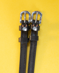 Black leather ManeJane spur straps with silver buckles and grey donkey face charms on yellow